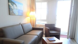 Moderni hotellihuone, jossa on sohva, nojatuoli ja pieni pöytä, jonka päällä on kirja.