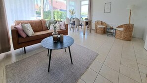 A living room with a sofa, a round coffee table, wicker chairs, and a dining table.