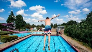 A person jumping off a pool with a clear sky and trees in the background.