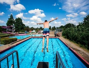 A person jumping off a pool with a clear sky and trees in the background. - Stay in the Heart of South Beveland (Heinkenszand)