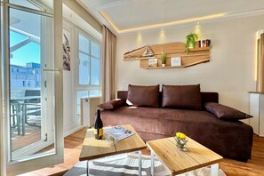 A modern living room with a brown sofa, wooden coffee tables, and a large window. - Ferienwohnung in Sellin mit Balkon in Südostlage (Sellin)