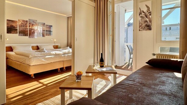 Een moderne hotelkamer met een bed, een kleintje tafeltje met een fles, een sofa en een balkon met een stoel.