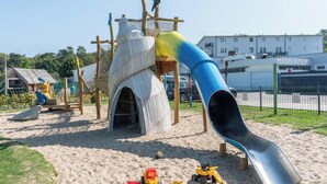 Une aire de jeux avec un toboggan, des structures d’escalade et du sable.