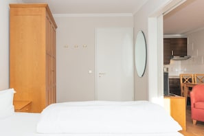 A bedroom with a bed, wooden wardrobe, a door, and a kitchen visible through an open door. - Ferienwohnung Sellin auf Rügen mit Balkon (Sellin)
