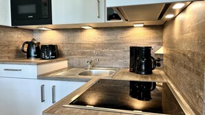 A compact kitchen with a microwave, coffee maker, and electric kettle on the countertop, a sink, and a built-in stovetop. - Urlaub im Seepark Sellin (Sellin)