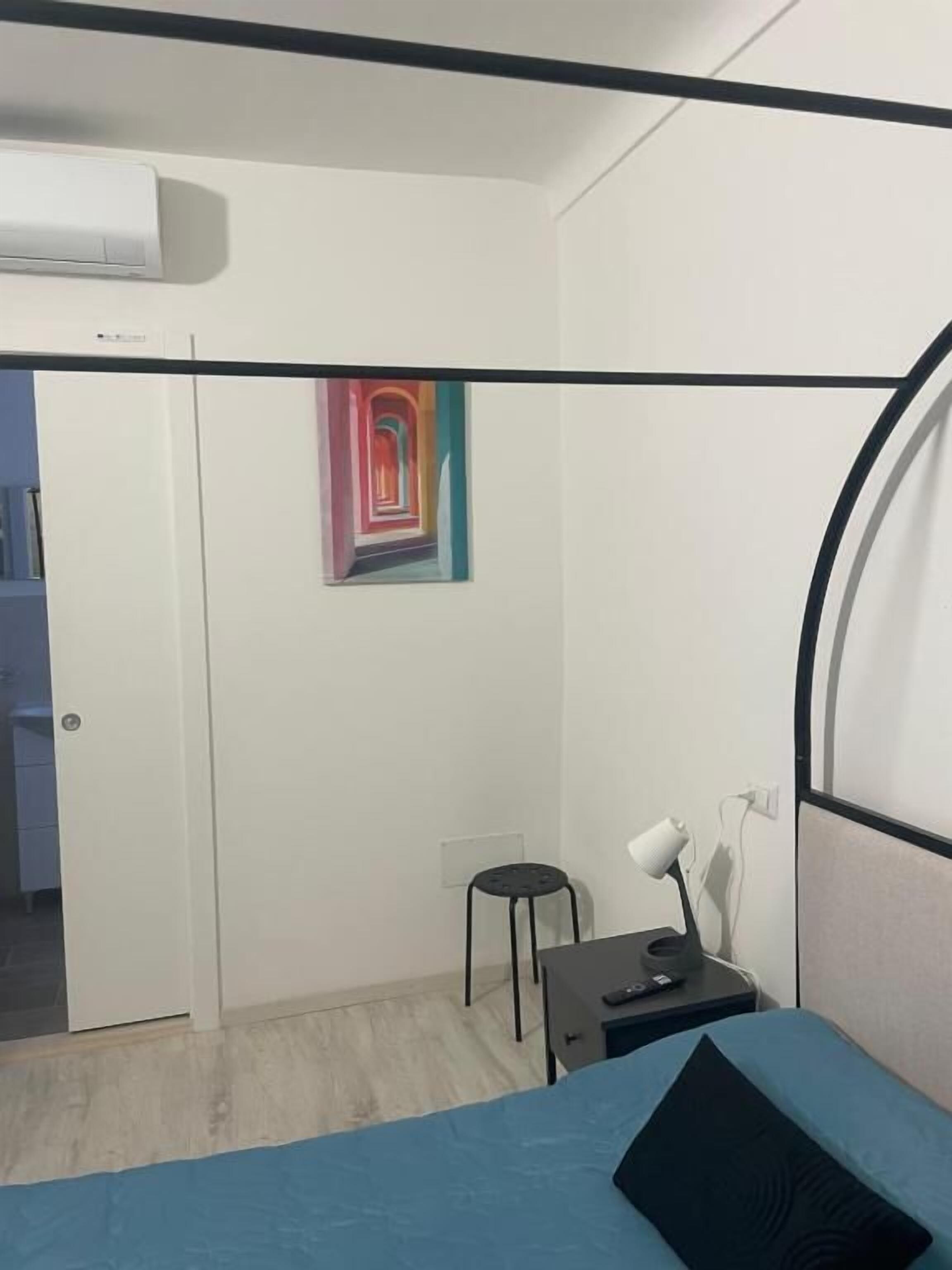 Un dormitorio con una cama litera, un escritorio con una silla, un aire acondicionado de pared y un cuadro de colores.