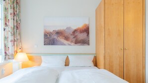 A bedroom with a bed, a wooden wardrobe, a wall-mounted painting, and a window with curtains. - Ferienwohnung in Sellin mit Balkon und WLAN (Sellin)