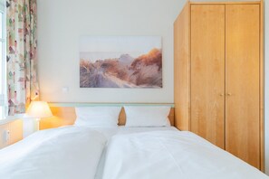 A bedroom with a bed, a wooden wardrobe, a wall-mounted painting, and a window with curtains. - Ferienwohnung in Sellin mit Balkon und WLAN (Sellin)