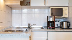 A kitchen with white cabinets, a stainless steel sink, a microwave, a coffee maker, and a kettle. - Ferienwohnung in Sellin mit Balkon und WLAN (Sellin)