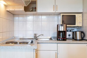 A kitchen with white cabinets, a stainless steel sink, a microwave, a coffee maker, and a kettle. - Ferienwohnung in Sellin mit Balkon und WLAN (Sellin)