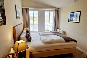 A bedroom with a bed, a bedside lamp, a window with curtains, and a picture on the wall. - Moderne Ferienwohnung mit Balkon und WLAN in Sellin (Sellin)
