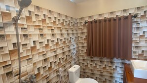 A bathroom with a tiled wall, a toilet, a shower, and a wooden vanity.