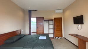 A bedroom with a bed, a desk, a TV, and a door leading to another room.