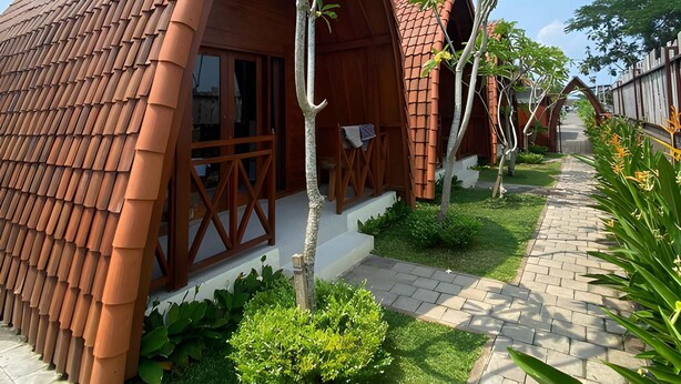 A row of rustic-style cabins with terracotta roofs, wooden balconies, and a paved pathway leading through a well-maintained garden.