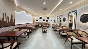 Un restaurante con una decoración moderna, que presenta una zona central de comedor con mesas y sillas, una pared estampada y adornos circulares en la pared.