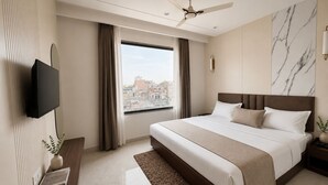 Una habitación de hotel moderna con una cama grande, un televisor de pantalla plana montado en la pared, un ventilador de techo y un ventanal con vistas a la ciudad.