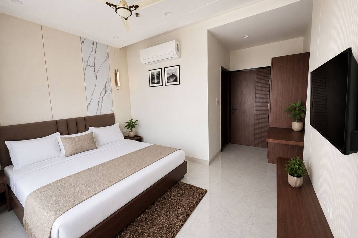 A modern bedroom with a large bed, a ceiling fan, an air conditioning unit, a TV, and a small potted plant.