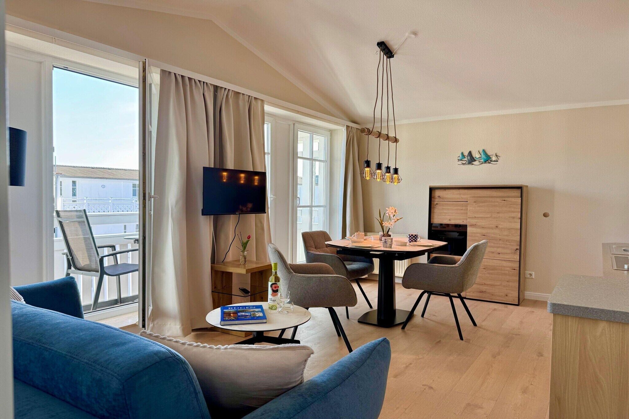 Una sala de estar moderna con un sofá, una mesa de comedor con sillas, un televisor y vistas al exterior.