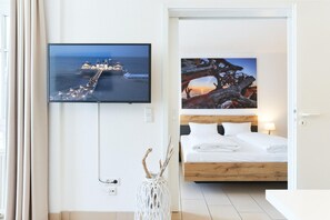 Un dormitorio con cama, televisión montada en la pared y un cuadro de un árbol.