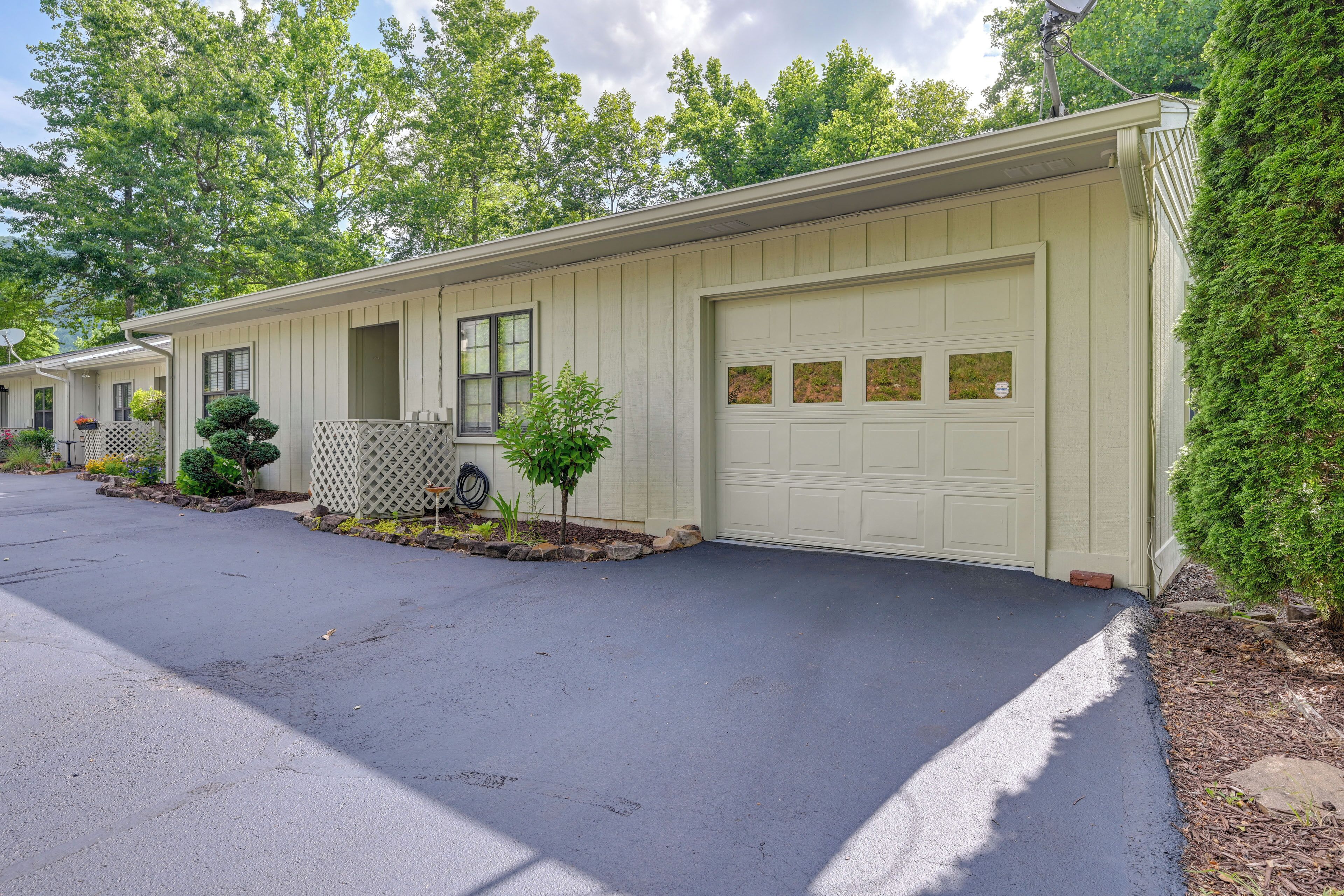 A row of single-story houses with attached garages, surrounded by trees and a clear driveway.
