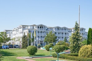 Ein großes, weißes, mehrgeschossiges Gebäude mit einer symmetrischen Fassade, umgeben von gepflegten Rasenflächen und Bäumen.