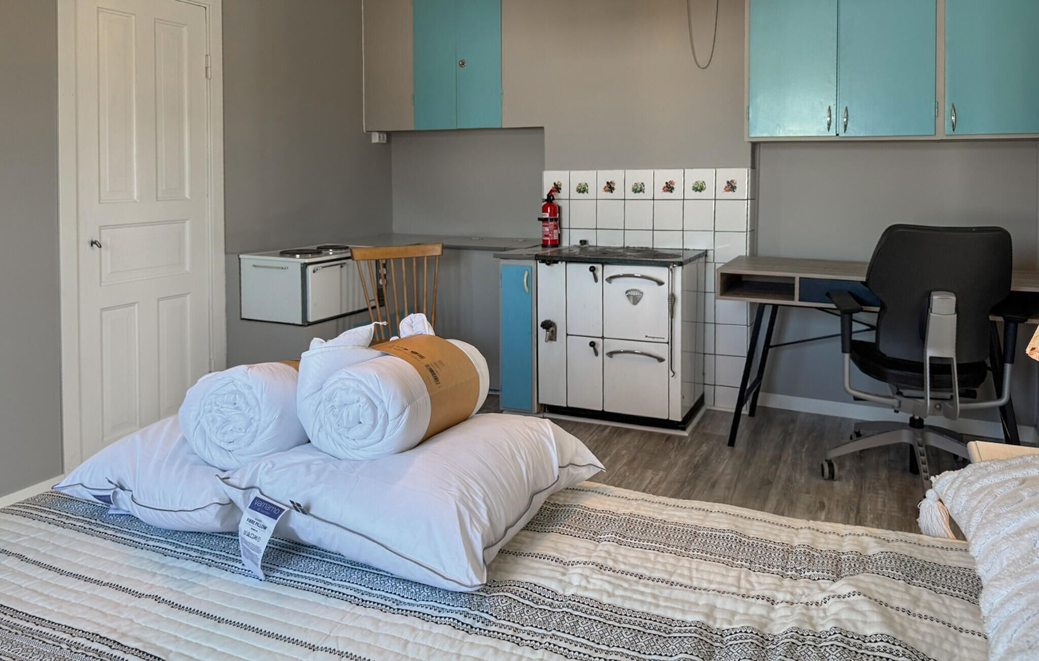 Habitació d'hotel senzilla amb llit, escriptori, cadira, petita cuina i armari.