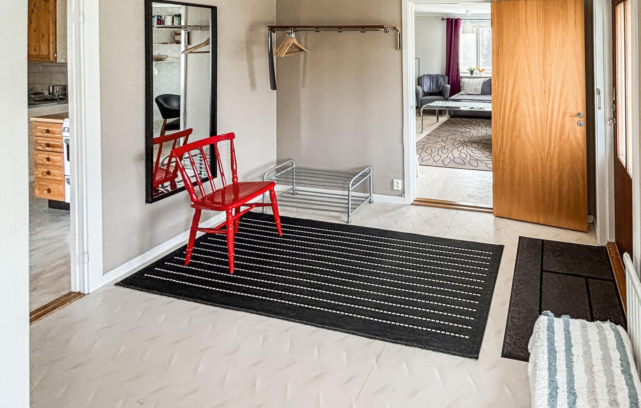 Un couloir avec une chaise rouge, un porte-manteau, un miroir et une porte donnant sur un salon.