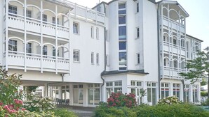 A multi-story hotel with balconies, large windows, and a garden area with flowers. - Schöne Ferienwohnung für 4 Personen ostseenah in Sellin (Sellin)