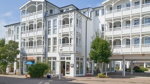 A multi-story building with balconies and large windows, a paved area in front, and a sign for a restaurant. - Schöne Ferienwohnung für 4 Personen ostseenah in Sellin (Sellin)