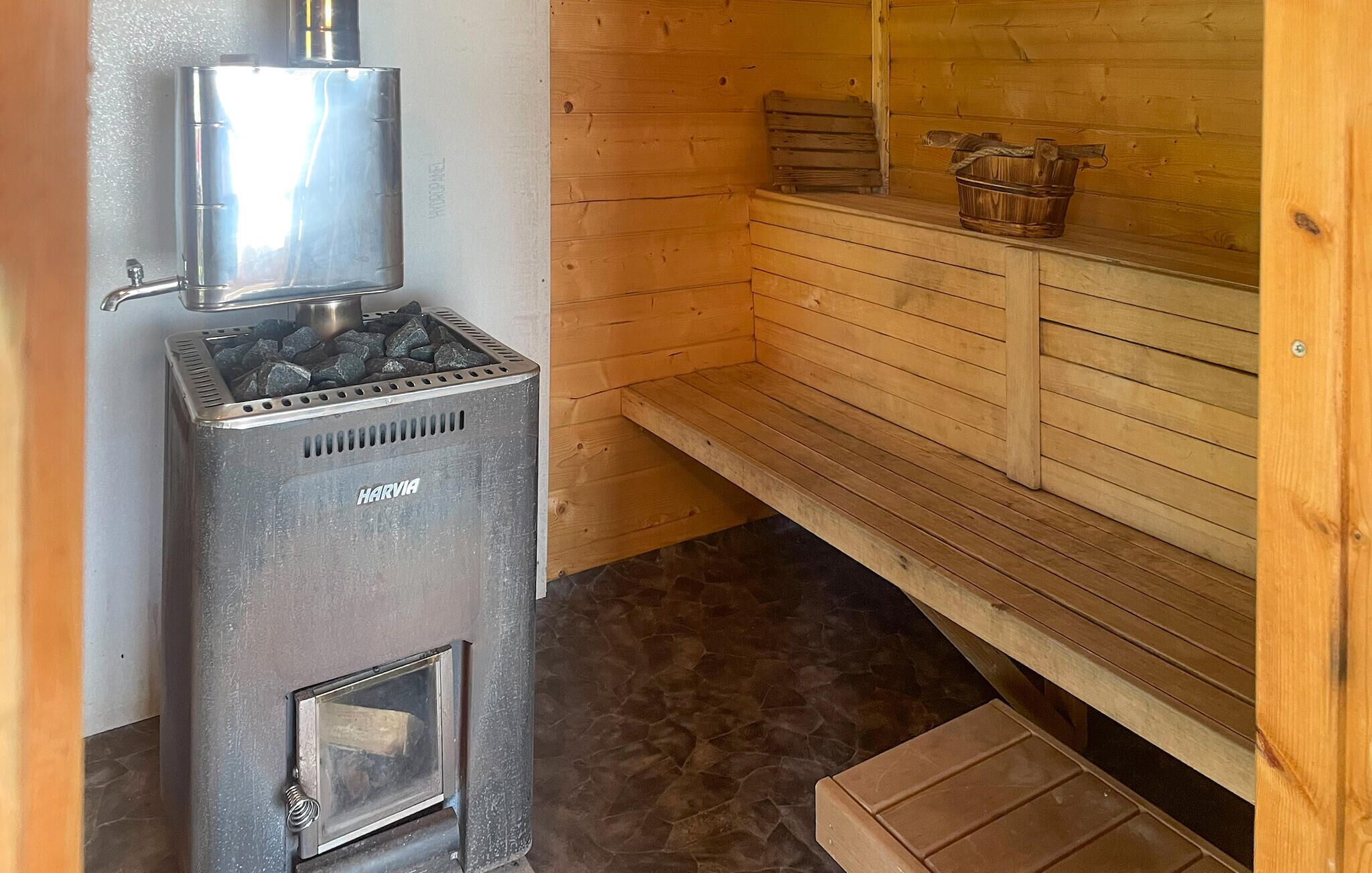 Uma sauna com aquecedor de metal, bancos de madeira e chão de pedra.