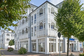 Ein weißes Gebäude mit mehreren Balkonen und großen Fenstern, umgeben von viel Grün.