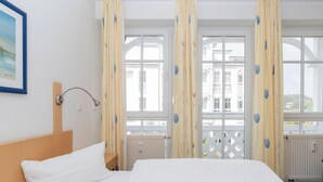 Une chambre d’hôtel avec un lit, une table de chevet, une fenêtre avec des rideaux et une vue sur des immeubles.