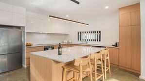 Una cocina moderna con una isla central, taburetes de bar, un refrigerador de acero inoxidable y armarios de madera.