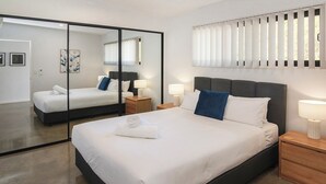 Una habitación de hotel moderna con una cama grande, mesitas de noche, un espejo y una ventana con persianas.