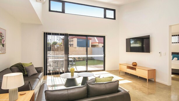Una sala de estar moderna con sofá, mesa de centro, televisor y puerta corrediza de vidrio a un jardín.