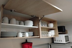 A kitchen with wooden shelves holding plates, bowls, and glasses, and a microwave on the counter. - Mobile home near Château de Chaumont (Onzain)