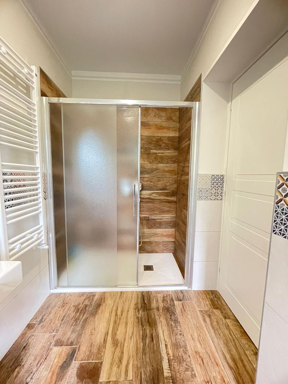 Un bagno con cabina doccia, pavimento in legno e piastrelle decorate.