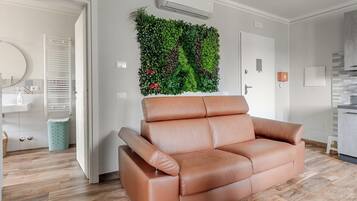 Ein modernes Wohnzimmer mit einer braunen Ledersofa, einer vertikalen Grünwand und einer Küchenzeile im Hintergrund.