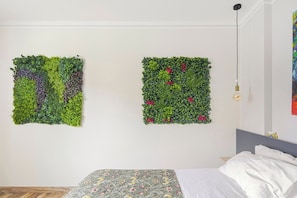 A room with a bed, a wall-mounted light fixture, and two square wall decorations with greenery and flowers. - Residence Maratta 54 Orchidea (Terni)