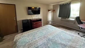 A hotel room with a bed, a TV mounted on the wall, a desk with a chair, and a window with curtains.