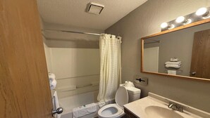 A bathroom with a toilet, sink, mirror, shower curtain, and towel rack. - 2 Full Beds | Non-Smoking (Coldwater, MI)