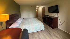 Una habitación de hotel con cama, cómoda, televisor y una silla.