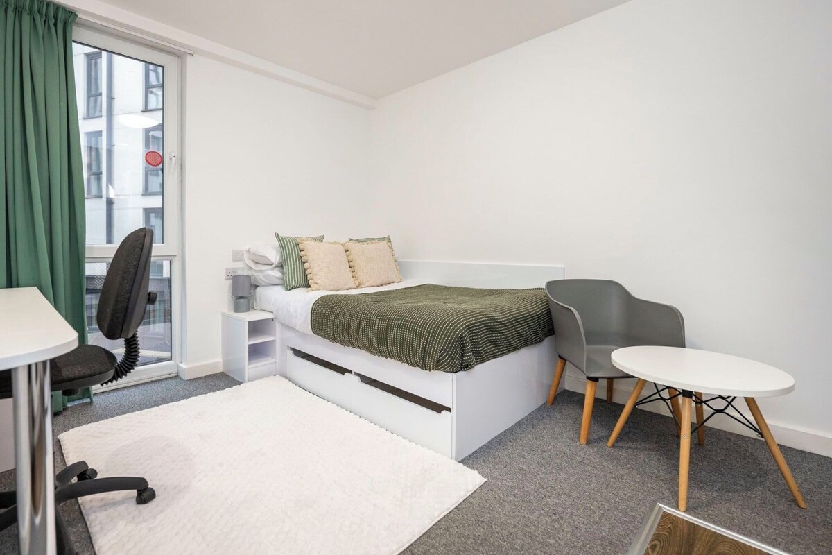 Ein kleines Schlafzimmer mit Bett, Schreibtisch, Stuhl und Nachttisch.