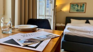Hotelkamer met een bed, een eettafel met een tijdschrift, een glas water en een raam met gordijnen.