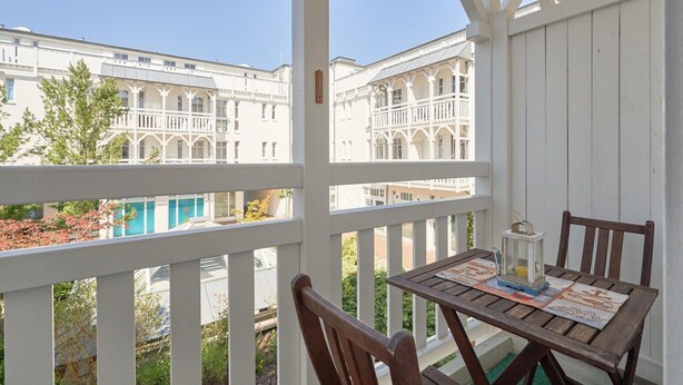Een balkon met een houten tafel en stoelen, met uitzicht op een zwembad en gebouwen.