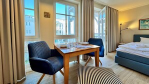 Een hotelkamer met een bed, een eettafel met stoelen, een raam met gordijnen en een lamp.
