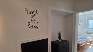 Ein Zimmer mit einem schwarzen Schrank, einer kleinen Topfpflanze und einem Wandschild mit der Aufschrift 'Zeit zum Entspannen'.