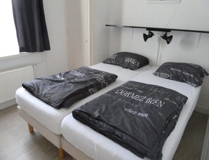 Ein Doppelbett mit schwarzer Bettwäsche mit Aufdruck, einem weißen Lattenrost und einem Holzboden.