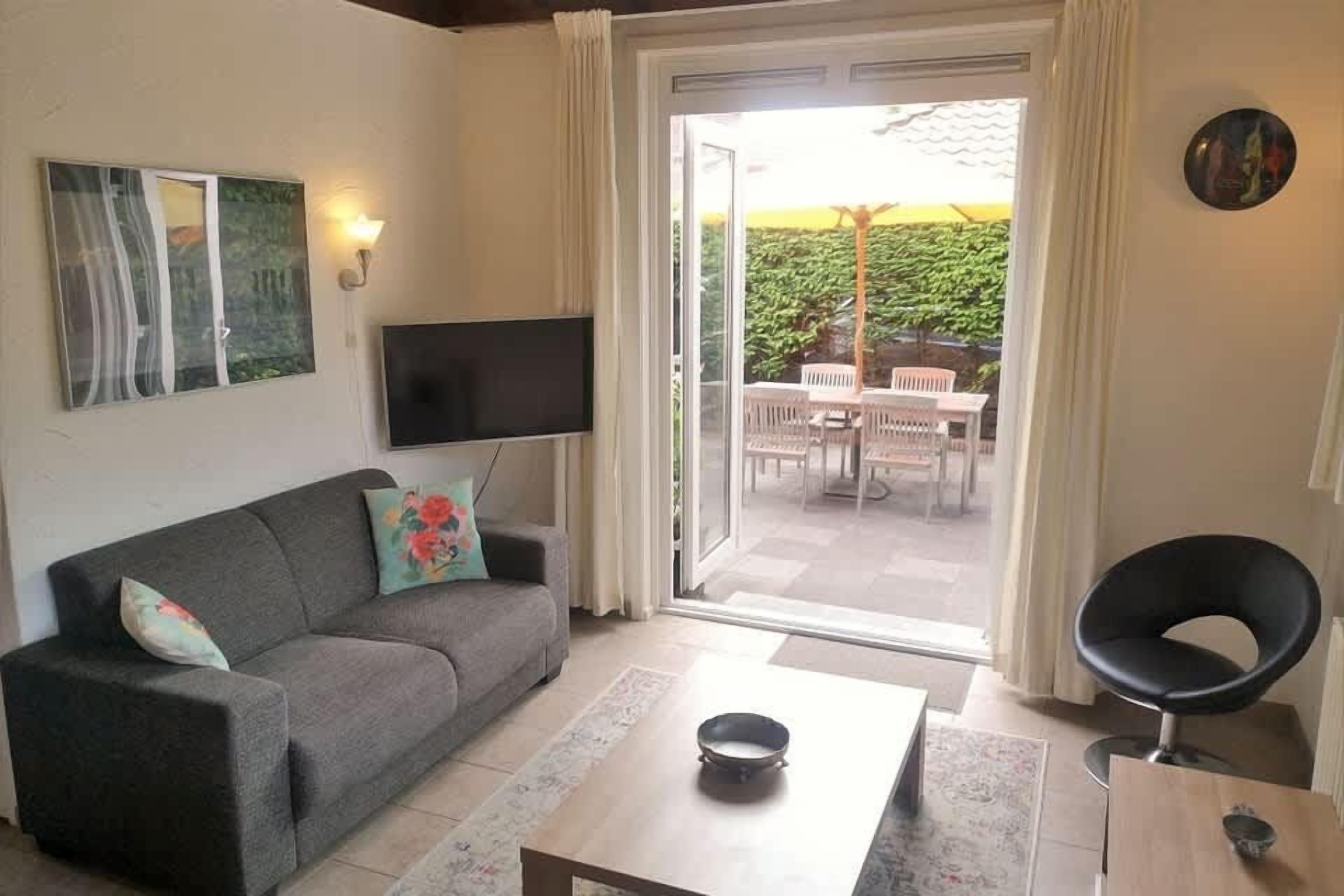 A living room with a sofa, a coffee table, a TV, and a sliding glass door leading to an outdoor area with a table and chairs.