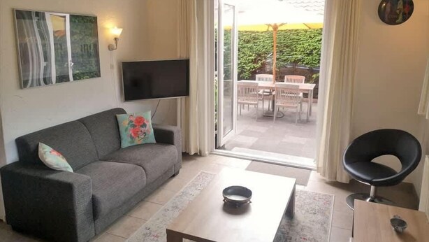 A living room with a sofa, a coffee table, a TV, and a sliding glass door leading to an outdoor area with a table and chairs. - Holiday Home 3 Minutes from Beach in Domburg - Ooststraat 16 (Domburg)